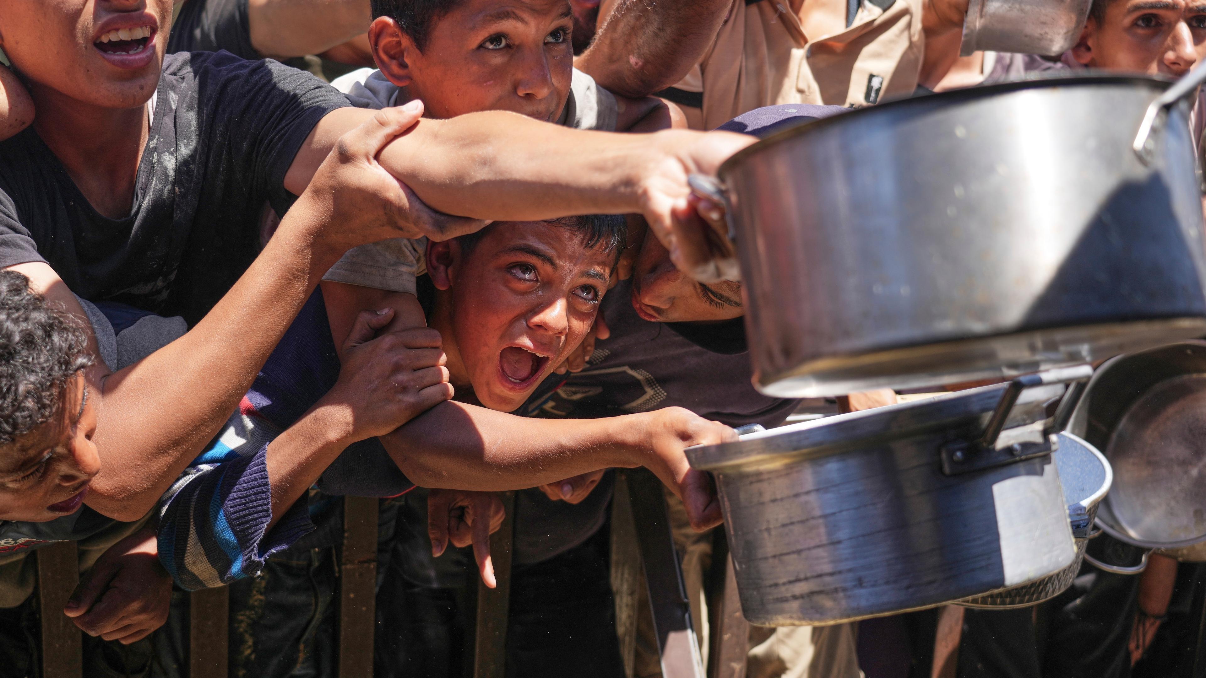 Palestinians struggle to receive cooked food distributed at a community kitchen in the Muwasi area of Khan Younis, in the Gaza Strip, Friday, May 23, 2025.
