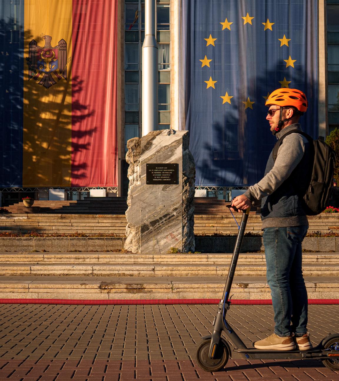 Mann auf einem Elektroroller vor Regierungsgebäude mit Moldau- und Europaflagge