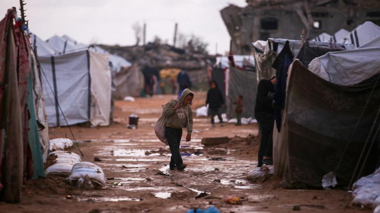 Ein Kind läuft durch ein nasses, zerstörtes Zeltlager. 