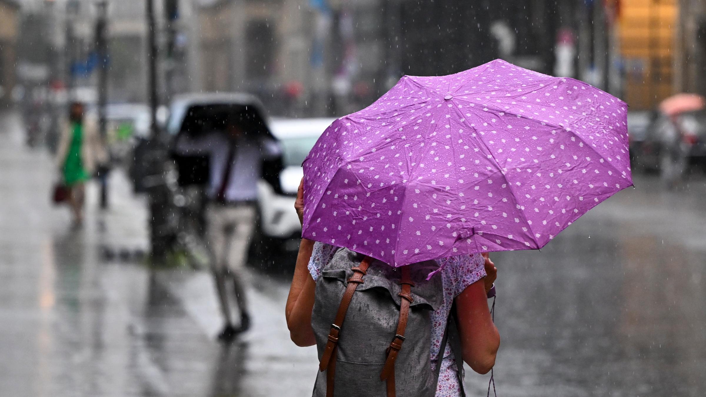 Berlin: Passanten am Gendarmenmarkt versuchen sich gegen die heftigen Regenfälle zu schützen. Starkregen bestimmt in den nächsten Stunden das Wettergeschehen