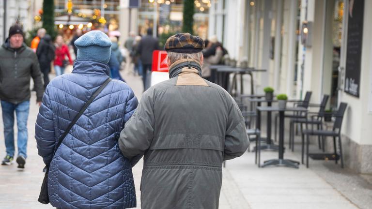 Ein älteres Paar geht Arm in Arm durch eine Einkaufsstraße.