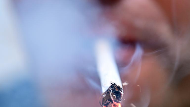 Person raucht eine glühende Zigarette