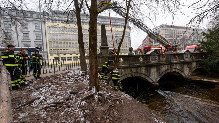 Mitarbeiter der Berufsfeuerwehr bauen in Anwesenheit von Polizeibeamten die diversen Einbauten und Vorrichtungen für eine künstliche Welle am Eisbach wieder ab.