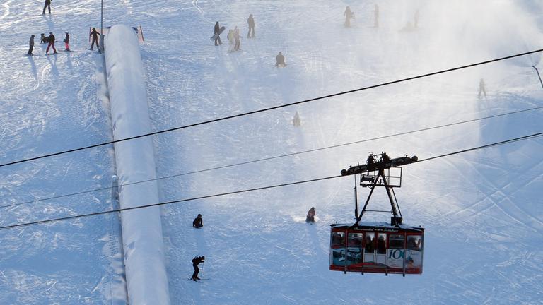 Blick auf die Gondel einer Seilbahn während Wintersportler auf einer Piste des Fichtelbergs unterwegs sind. In Sachsens größtem alpinen Skigebiet ist der Skibetrieb gestartet. Erst am Dienstag wurde dort ein erster Lift in Betrieb genommen, Silvester sollen weitere folgen