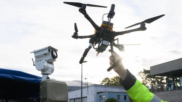 Ein DLR-Mitarbeiter hält eine Drohne vor einem Fahrzeug zur Drohnendetektion