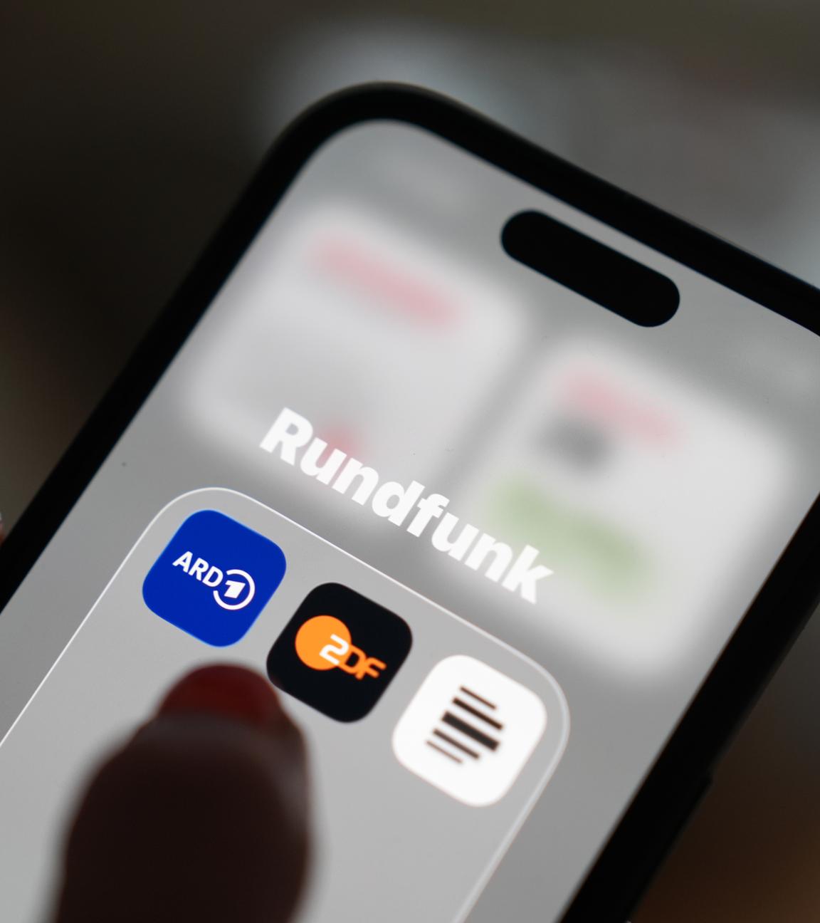 Auf dem Bildschirm eines Smartphones sind die App-Icons von ARD, ZDF und Deutschlandfunk im Ordner «Rundfunk» zu sehen