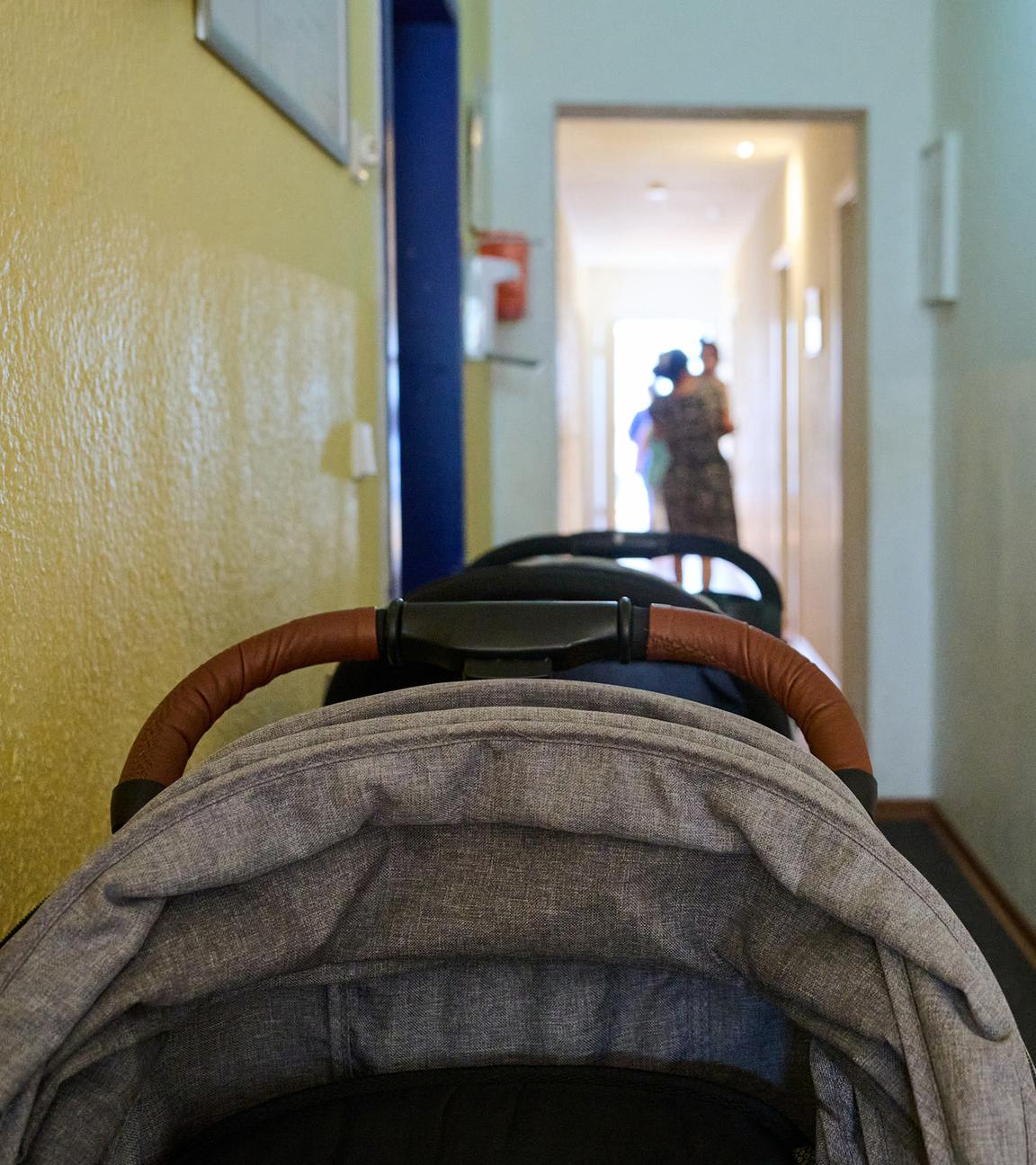 In einem Frauenhaus stehen Kinderwagen im Flur, während eine Mutter mit ihren Kindern am Ende des Flurs entlanggeht.