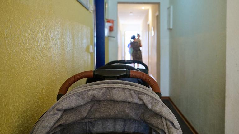 In einem Frauenhaus stehen Kinderwagen im Flur, während eine Mutter mit ihren Kindern am Ende des Flurs entlanggeht.