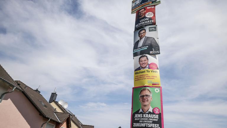 Wahlplakate verschiedener Kandidaten hängen an einem Laternenpfahl.