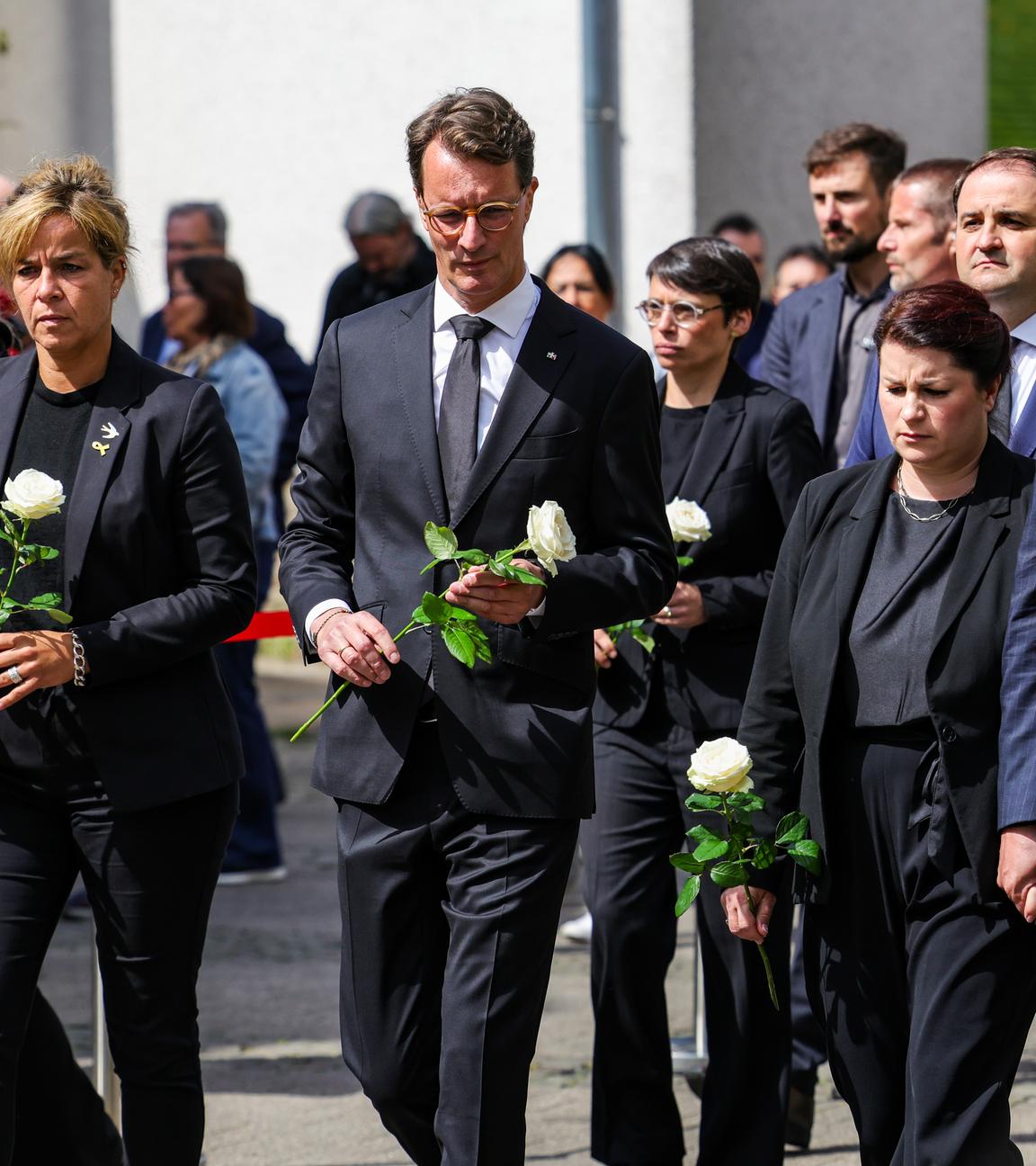 Mona Neubaur (Bündnis 90/Grüne, l-r), Ministerin für Wirtschaft, Industrie, Klimaschutz und Energie von Nordrhein-Westfalen, Hendrik Wüst (CDU), Ministerpräsident von Nordrhein-Westfalen, Josefine Paul (Bündnis 90/Grüne), Ministerin für Familie und Integration von Nordrhein-Westfalen, Ursula Linda Kurzbach und Tim Kurzbach, Oberbürgermeister der Stadt Solingen, haben weiße Rosen in den Händen und gehen zum Gedenkstein.