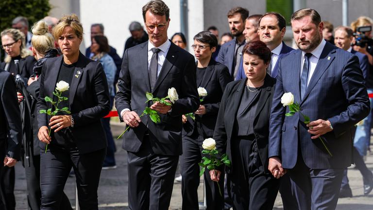 Mona Neubaur (Bündnis 90/Grüne, l-r), Ministerin für Wirtschaft, Industrie, Klimaschutz und Energie von Nordrhein-Westfalen, Hendrik Wüst (CDU), Ministerpräsident von Nordrhein-Westfalen, Josefine Paul (Bündnis 90/Grüne), Ministerin für Familie und Integration von Nordrhein-Westfalen, Ursula Linda Kurzbach und Tim Kurzbach, Oberbürgermeister der Stadt Solingen, haben weiße Rosen in den Händen und gehen zum Gedenkstein.