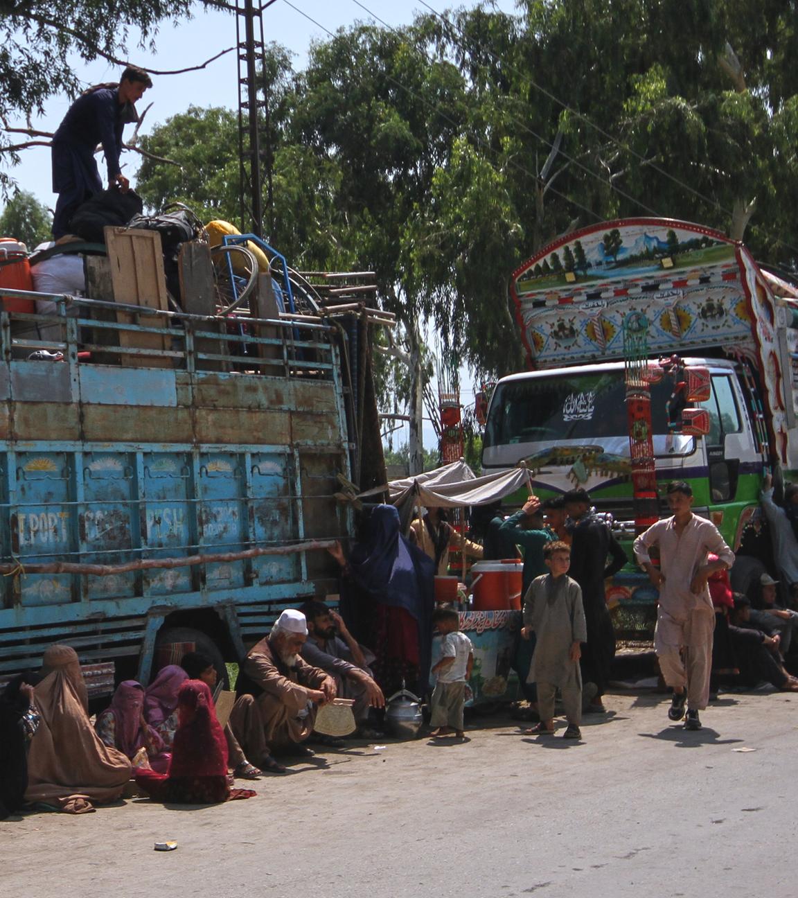 Afghanische Flüchtlingsfamilien, die auf dem Weg zurück in ihr Heimatland sind, versammeln sich neben Lastwagen in Pakistan am 25.08.2025