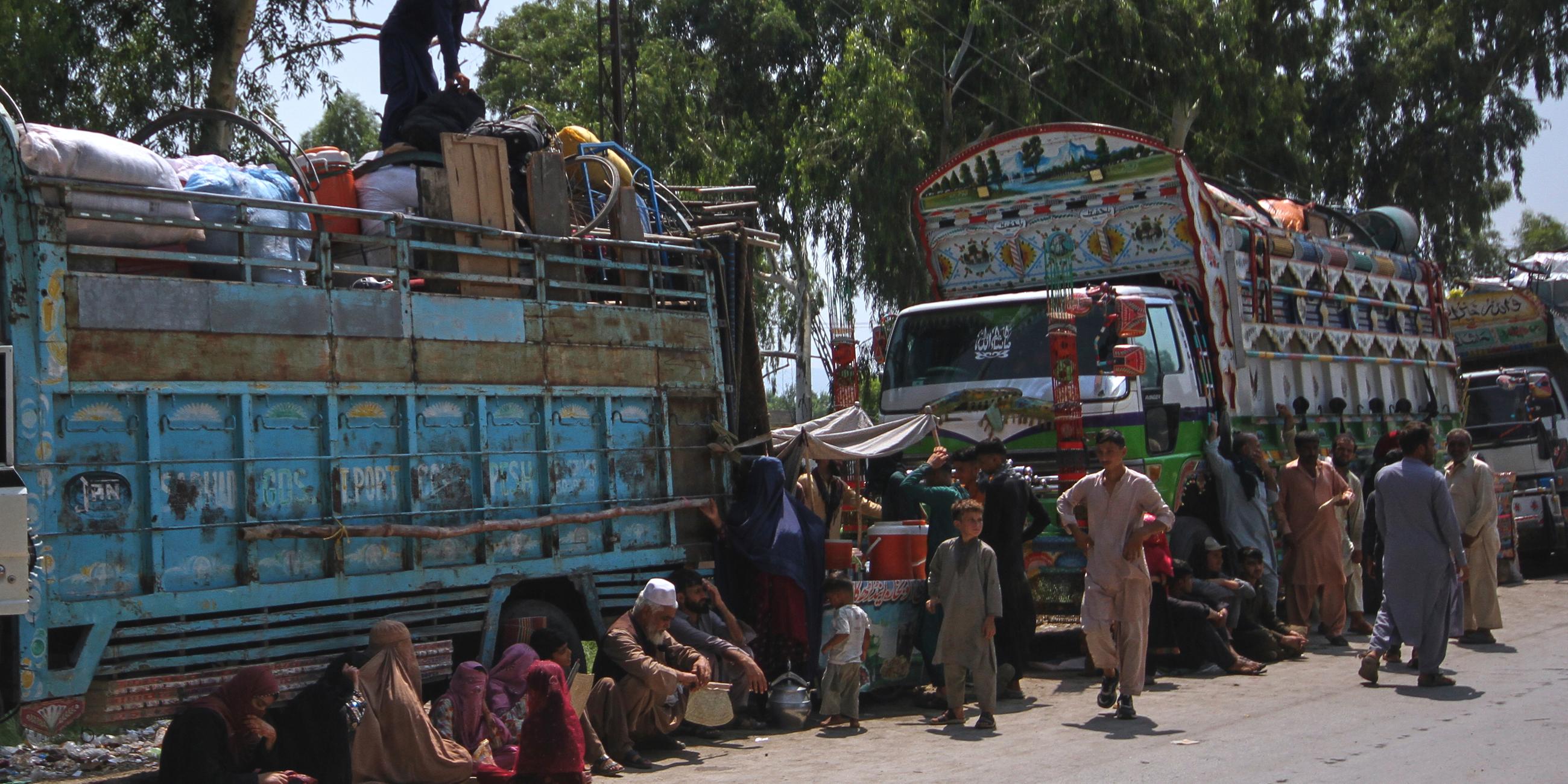 Afghanische Flüchtlingsfamilien, die auf dem Weg zurück in ihr Heimatland sind, versammeln sich neben Lastwagen in Pakistan am 25.08.2025
