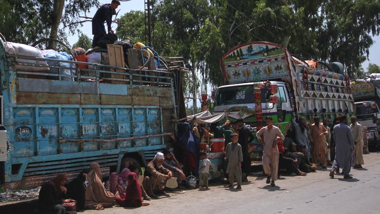 Afghanische Flüchtlingsfamilien, die auf dem Weg zurück in ihr Heimatland sind, versammeln sich neben Lastwagen in Pakistan am 25.08.2025