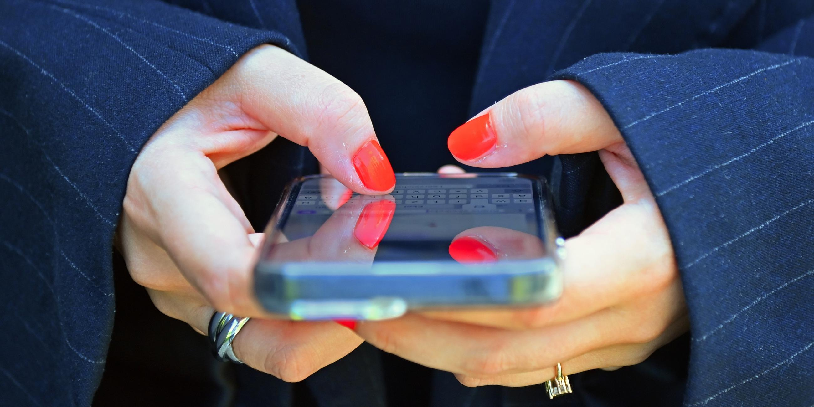 Frau mit lackierten Fingernaegeln tippt in ihr Smartphone