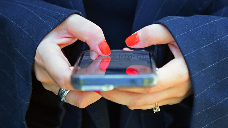 Frau mit lackierten Fingernaegeln tippt in ihr Smartphone