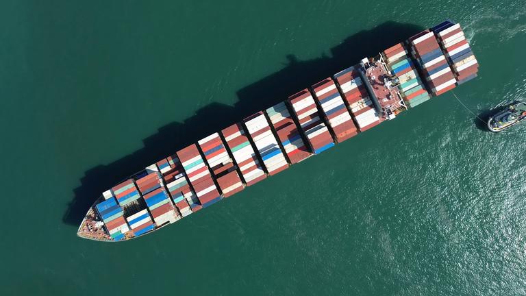 Draufsicht auf ein großes, mit bunten Containern gefülltes Frachtschiff; abschluss; anschluss; ausruestung; basspfeife; behälter; boot; bunten; container; containerhafen; containern; dock; draufsicht; draussen; fracht; frachtschiff; gefülltes; globalisierung; großes; hafen; handel; industrie; kommerziell; konjunktur; lieferkette; logistik; luftbildaufnahme; marin; marine; maritim; meer; navigation; ozean; schlepper; tag; top; transport; transportieren; umschlag; wachstum; wasserfahrzeug; wirtschaft; über