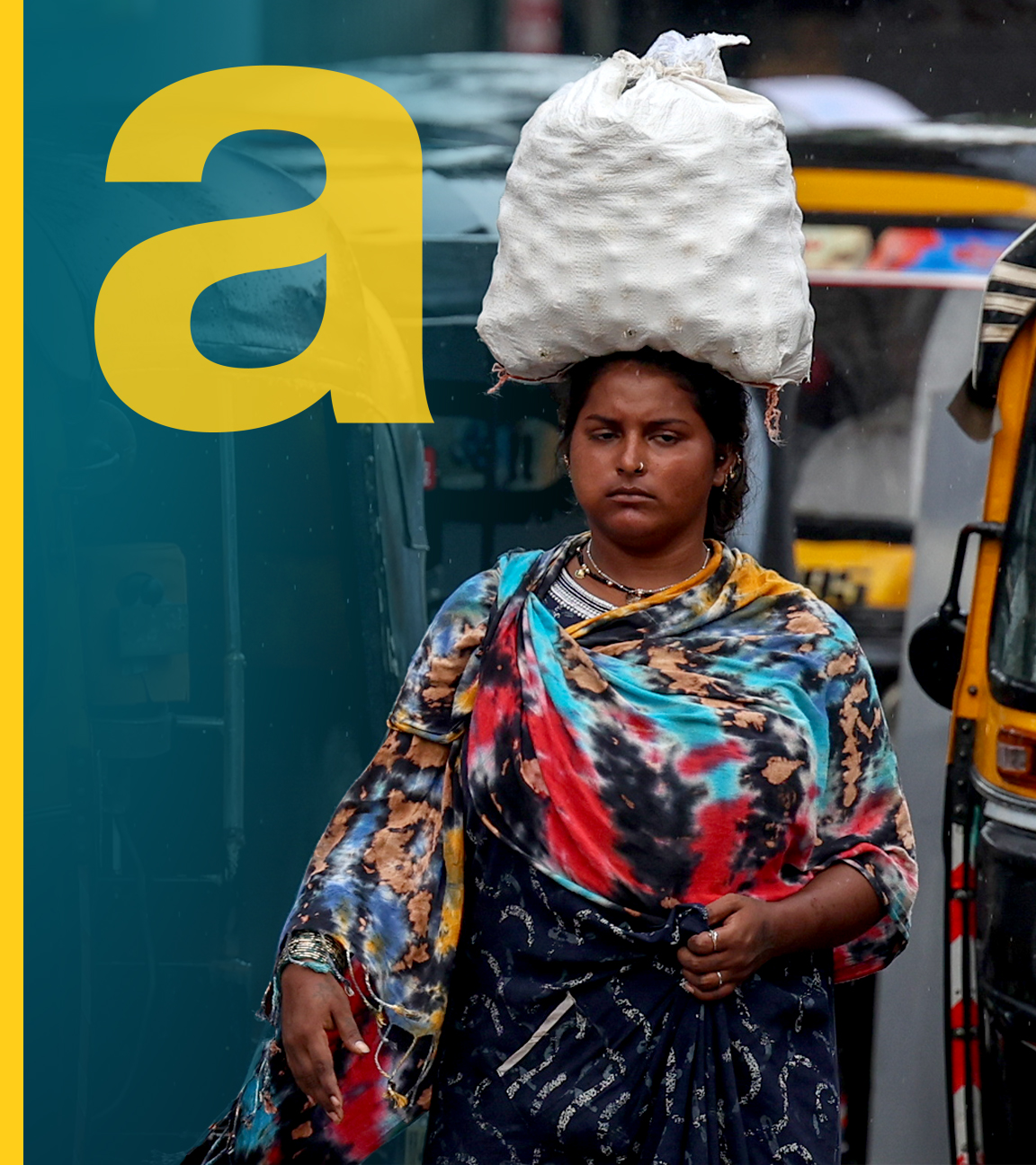 Man erkennt eine indische Frau, die auf dem Kopf Waren trägt zwischen Tuktuks.