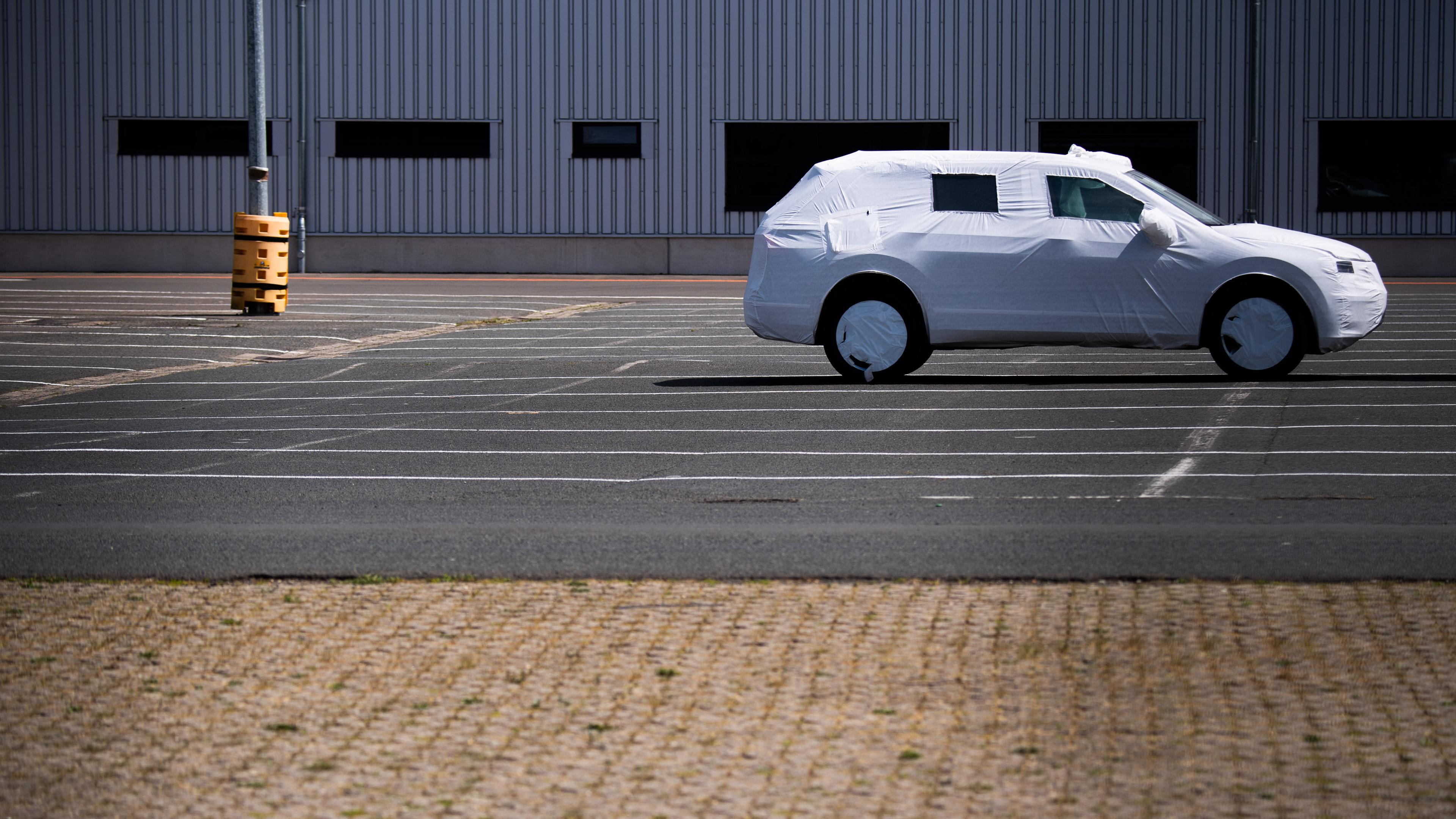 Ein einzelnes in Plane verpacktes Neufahrzeug steht auf einem Parkplatz. 