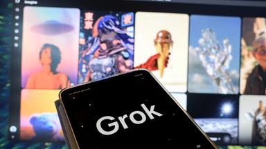 Grok auf dem Handy vor dem Laptopbildschirm