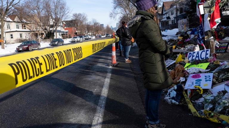 Menschen besuchen stehen an der gedenkstätte von Renee Good. Polizei-Absperrband ist im Vordergrund zu sehen