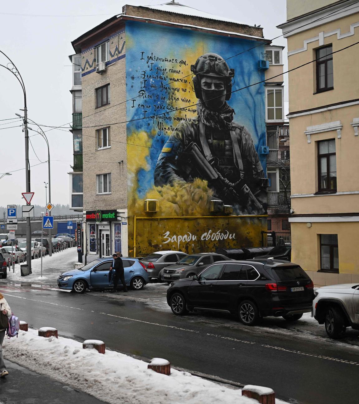Fußgänger laufen an einem Mural vorbei, das einen Ukrainischen Soldaten vor blau weißem Hintergrund zeigt