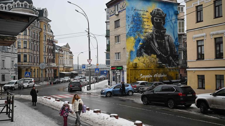 Fußgänger laufen an einem Mural vorbei, das einen Ukrainischen Soldaten vor blau weißem Hintergrund zeigt