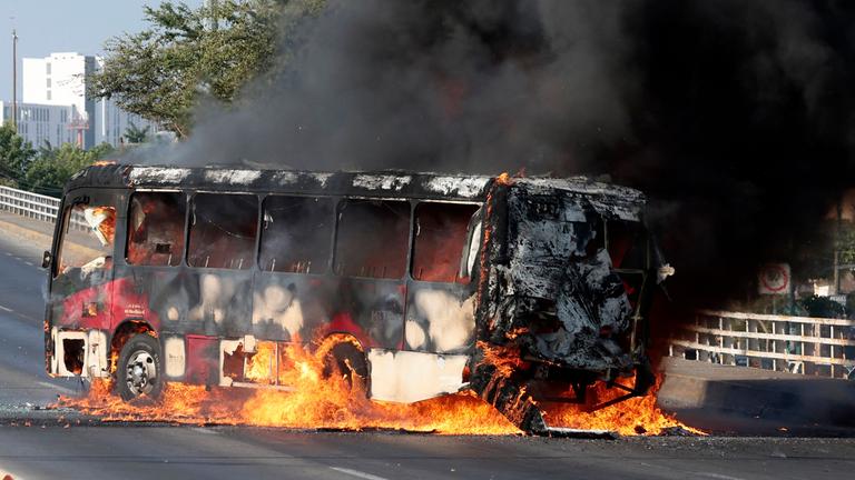 Ein Mitglied der Generalstaatsanwaltschaft steht am 22. Februar 2026 in einer der Hauptstraßen von Zapopan im mexikanischen Bundesstaat Jalisco Wache neben einem Bus, der von organisierten kriminellen Gruppen als Reaktion auf eine Operation in Jalisco zur Festnahme einer hochrangigen Zielperson in Brand gesetzt wurde. Bewaffnete Zivilisten blockierten mehrere Straßen im Bundesstaat Jalisco im Westen Mexikos nach einer Operation der Bundeskräfte in der Stadt Tapalpa, wie lokale Behörden berichteten. Jalisco, wo vier Spiele der bevorstehenden Weltmeisterschaft 2026 ausgetragen werden, ist die Heimat des mächtigen Jalisco New Generation Cartel (CJNG) und wurde in den letzten Jahren von mehreren Gewaltausbrüchen erschüttert