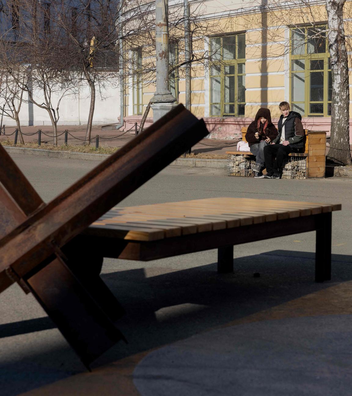 In Kiew sitzen Jugendliche auf einer Bank in der Nähe einer Metallbarriere.