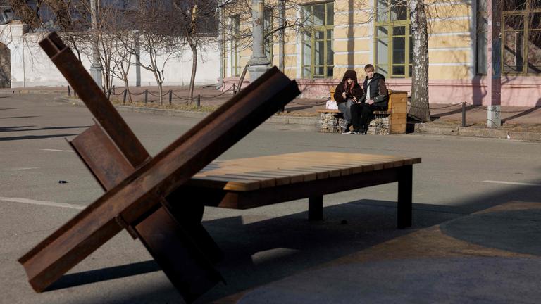 In Kiew sitzen Jugendliche auf einer Bank in der Nähe einer Metallbarriere.