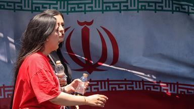 Women walk past Iran's national flag at the Vanak Square in Tehran on June 10, 2026. Iran's foreign ministry said on June 10 that the United States had damaged the ongoing international diplomatic effort to end the war, after more US strikes on targets in southern Iran. (Photo by ATTA KENARE / AFP)