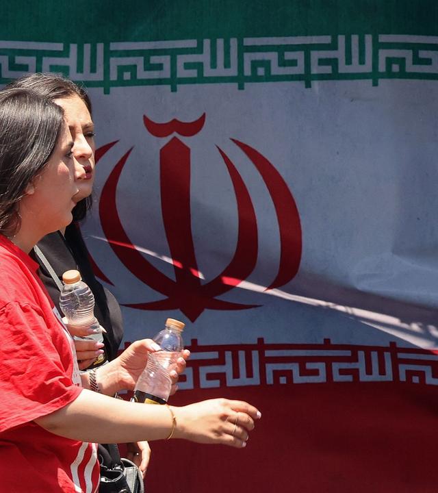 Women walk past Iran's national flag at the Vanak Square in Tehran on June 10, 2026. Iran's foreign ministry said on June 10 that the United States had damaged the ongoing international diplomatic effort to end the war, after more US strikes on targets in southern Iran. (Photo by ATTA KENARE / AFP)