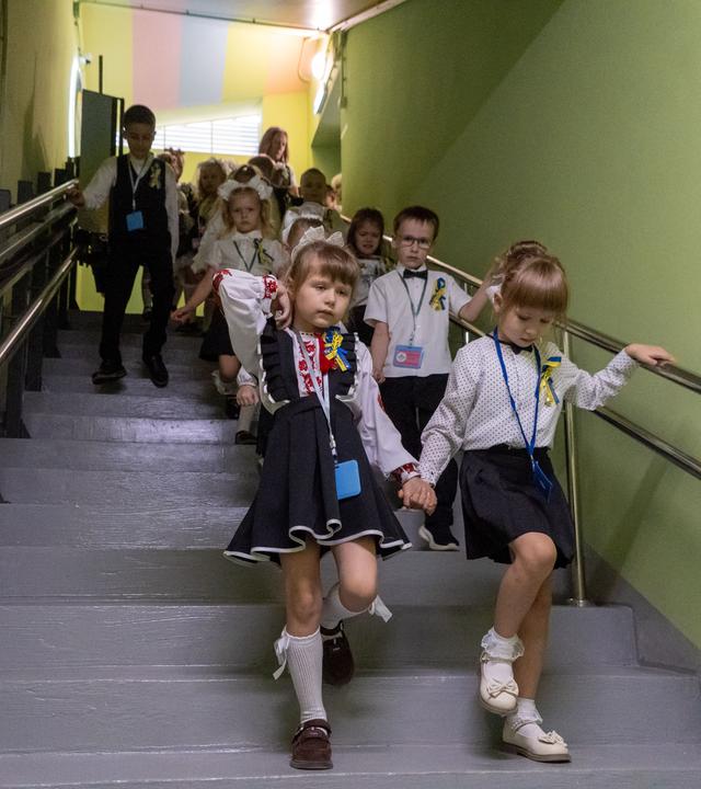 Schüler und Schülerinnen an ihren ersten Schultag nach den Sommerferien. Die Kinder gehen die Treppen runter zu ihrer Schule im Bunker. 
