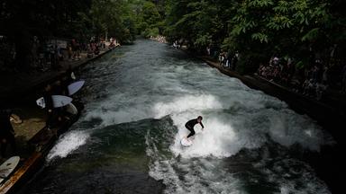 Ein Surfer reitet auf einer künstlichen Welle im Eisbach im Englischen Garten in München