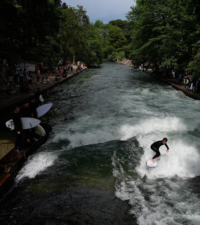 Ein Surfer reitet auf einer künstlichen Welle im Eisbach im Englischen Garten in München