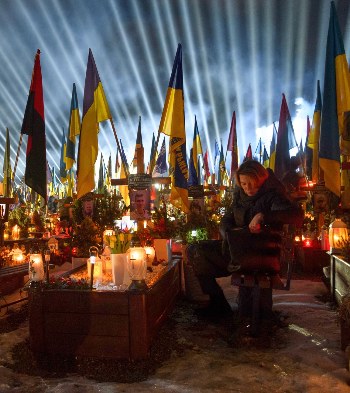 Flutlichter strahlen auf die Gräber der gefallenen Soldaten, während Menschen am Vorabend des vierten Jahrestags der vollständigen Invasion Russlands in Lemberg, Ukraine, am Montag, dem 23. Februar 2026, Kerzen anzünden.