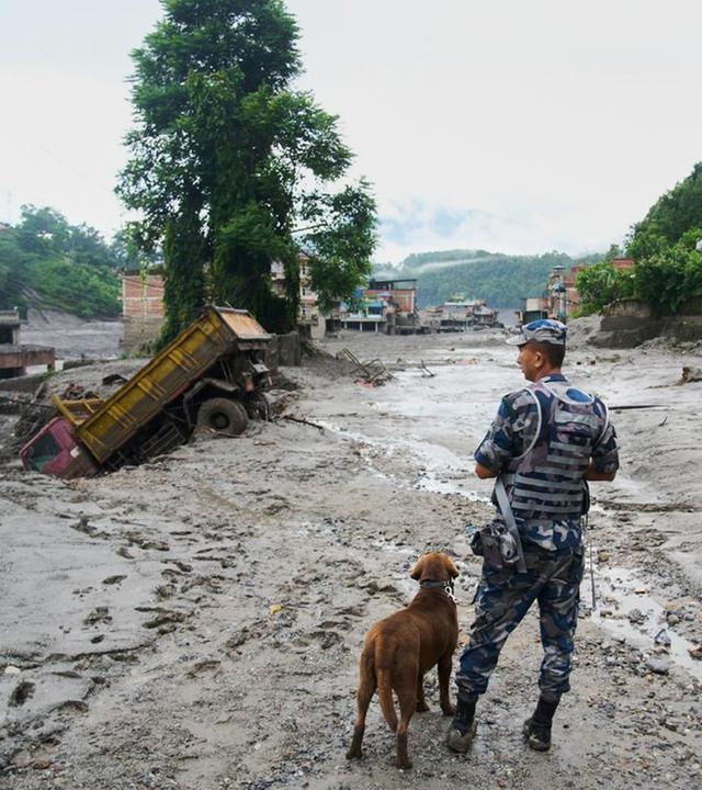 A policeman with a sniffer dog looks at the damage in the aftermath of flash floods in Devighat in the Nuwakot district in Nepal, Thursday, Aug 27, 2026.