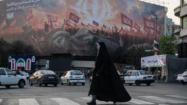 Teheran, Iran: Eone Frau überquert eine Straße, auf der ein großes Transparent die kollabierte Freiheitsstatue zeigt