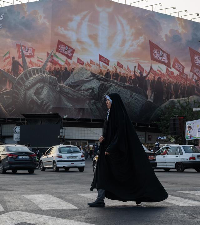 Teheran, Iran: Eone Frau überquert eine Straße, auf der ein großes Transparent die kollabierte Freiheitsstatue zeigt
