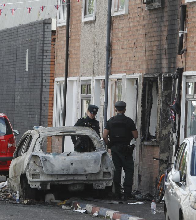 A view of burned-out vehicles and homes on a street as police takes measures in east Belfast, Northern Ireland, on June 10, 2026. Disorder continued across parts of Belfast following a knife attack that left a man seriously injured, with fires reported in several areas of the city during the unrest.