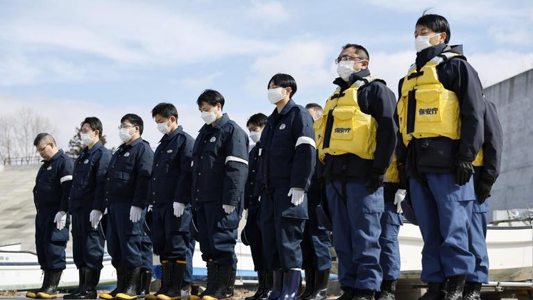 Polizeibeamte und Angehörige der japanischen Küstenwache halten am 11. März 2026, dem 15. Jahrestag des großen Ostjapan-Erdbebens, an einem Strand in Yamada in der Präfektur Iwate eine Schweigeminute ab. 