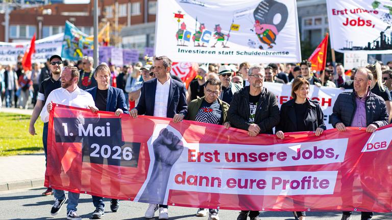 Olaf Lies (3.v.l,SPD), Ministerpräsident von Niedersachsen, hält zusammen mit anderen Teilnehmern einen Banner des Deutscher Gewerkschaftsbunds mit der Aufschrift: «1. Mai 2026; Erst unsere Jobs, dann eure Profite». Anlass sind bundesweite Kundgebungen der Gewerkschaften zum internationalen Tag der Arbeit.