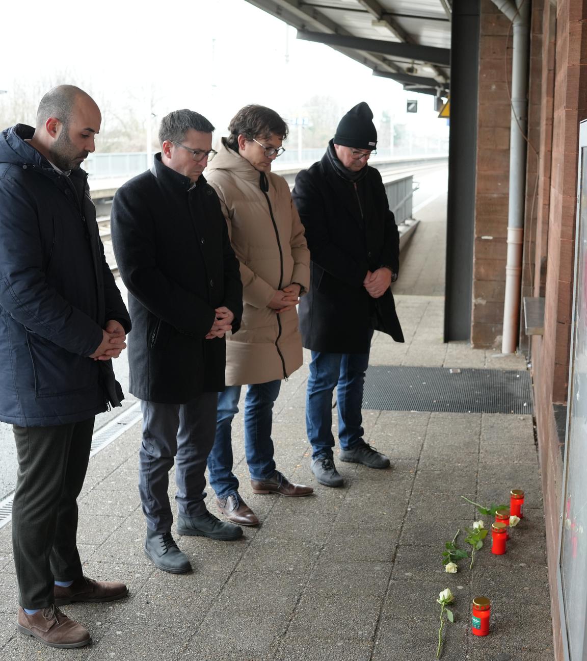 Menschen stehen vor Blumen und Kerzen am Bahnsteig im Gedenken an den Tod eines Zugbegleiters.