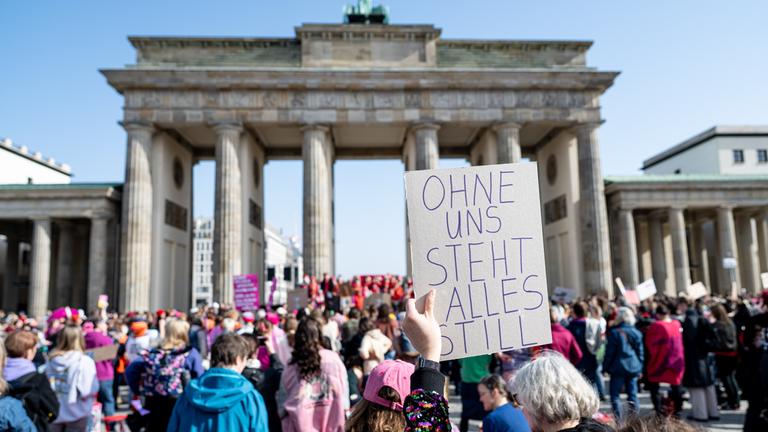 09.03.2026, Berlin: Eine Frau hält beim Aufruf zum weltweiten Frauen-Generalstreik bei einer Demonstration vor dem Brandenburger Tor ein Schild mit der Aufschrift ohne uns steht alles still hoch. Organisiert wir die Demo von einer in Berlin gegründeten Bewegung aus gut Hundert Frauen und einem Dutzend Männern, die für Frauenrechte eintritt