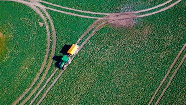 Ein Traktor fährt mit einen Streuwagen über ein Feld und verteilt Dünger. (Luftaufnahme mit einer Drohne). Das sonnige und trockene Wetter nutzen die Landwirte in Norddeutschland derzeit für anstehende Arbeiten auf den Äckern.