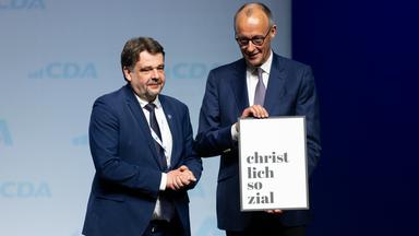 Bundeskanzler Friedrich Merz (r, CDU), hat als Dank für seinen Besuch von Dennis Radtke (CDU), CDA-Bundesvorsitzender ein Geschenk bekommen. Das Motto lautet "80 Jahre CDA - 80 Jahre soziale Marktwirtschaft"