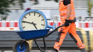 Ein Arbeiter transportiert eine Bahnhofsuhr auf einer Schubkarre. 