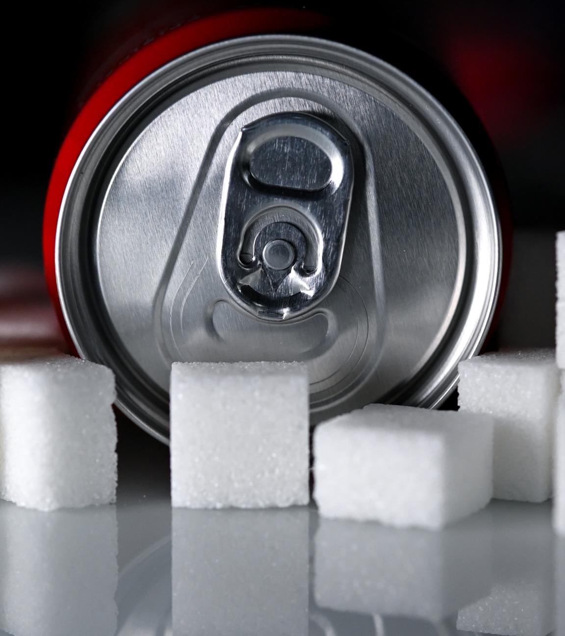 Eine Getränkedose mit einem Softdrink und zahlreiche Zuckerwürfel liegen auf einem Tisch.