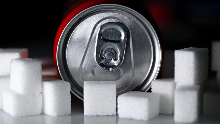 Eine Getränkedose mit einem Softdrink und zahlreiche Zuckerwürfel liegen auf einem Tisch.