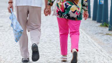 Zwei Mensche hand in hand eine Straße langlaufend von hinten betrachtet